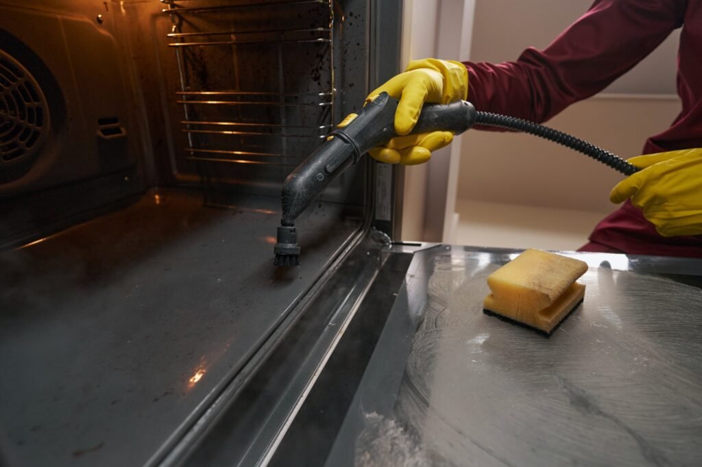 Professional janitor in rubber gloves cleaning kitchen appliance